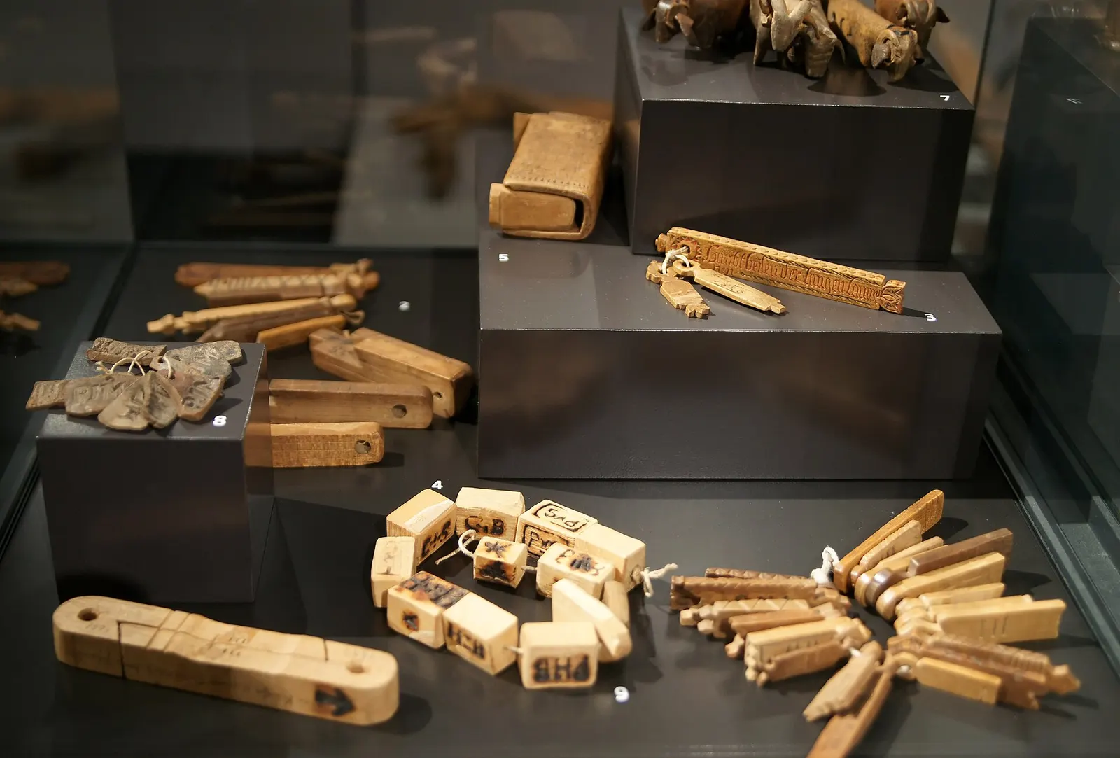 Old wooden tally sticks displayed in a museum case, each marked with notches and names.