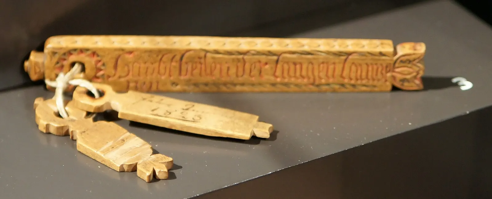 A carved and painted tally stick with two smaller wooden tags tied to it by a string.