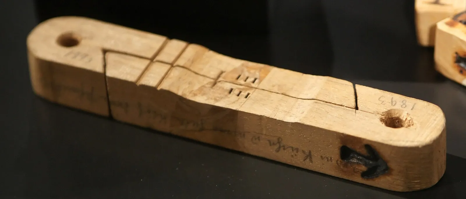 A wooden tally stick split lengthwise into two halves, with notches cut across the split and the year 1893 written at one end.